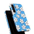 a blue phone case with a repeating pattern of white flowers on a black background.