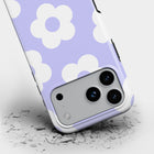 a smartphone case with a purple and white flower pattern, and it appears to be cracked or damaged, with pieces of the case scattered on the ground.